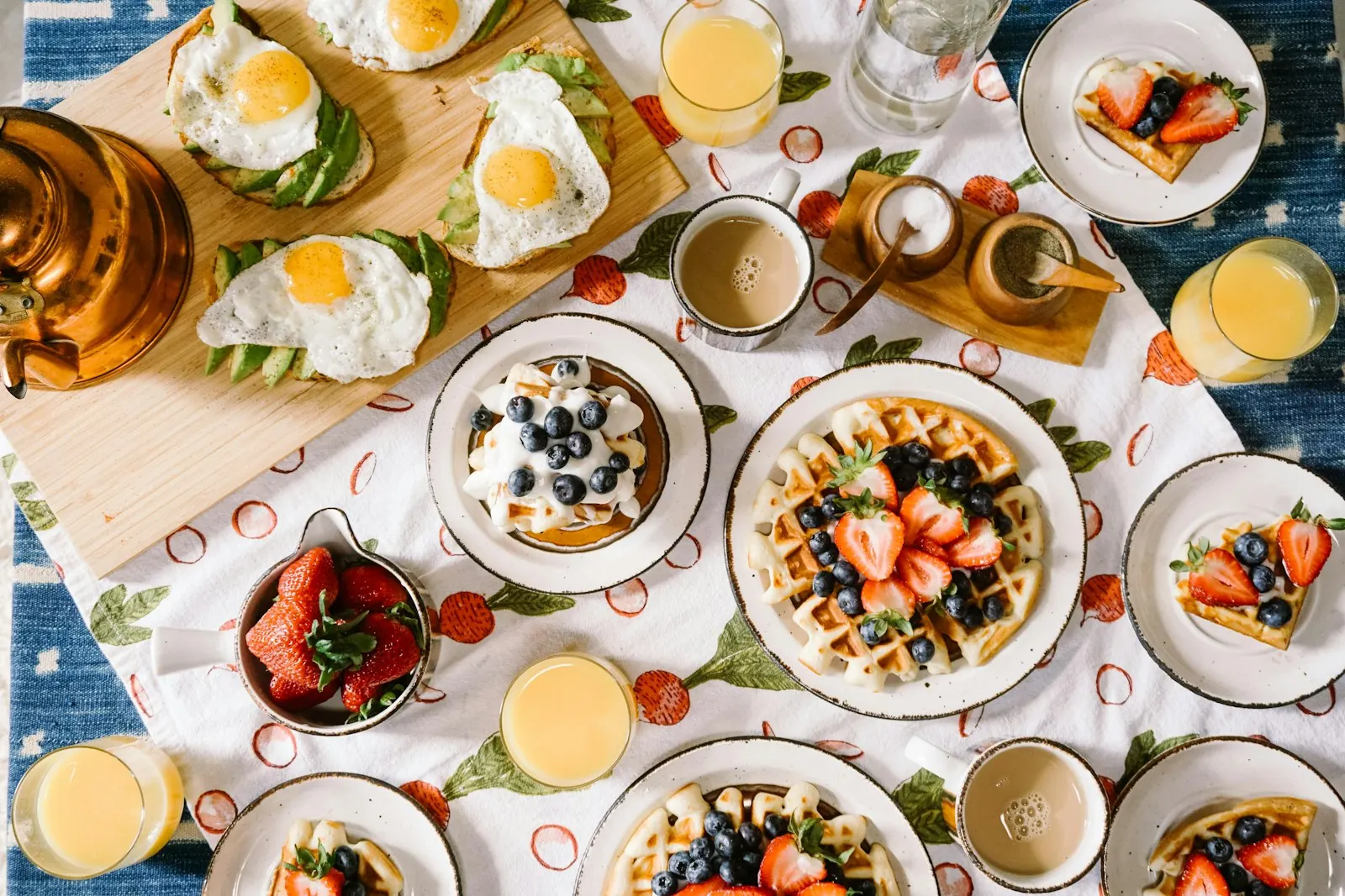 Overhead brunch table with waffles, fried-egg avo toast, berries, juice and coffee